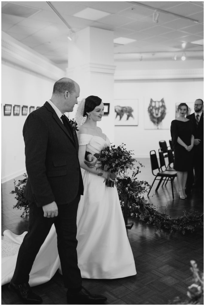 dad and bride walk down the aisle in black and white