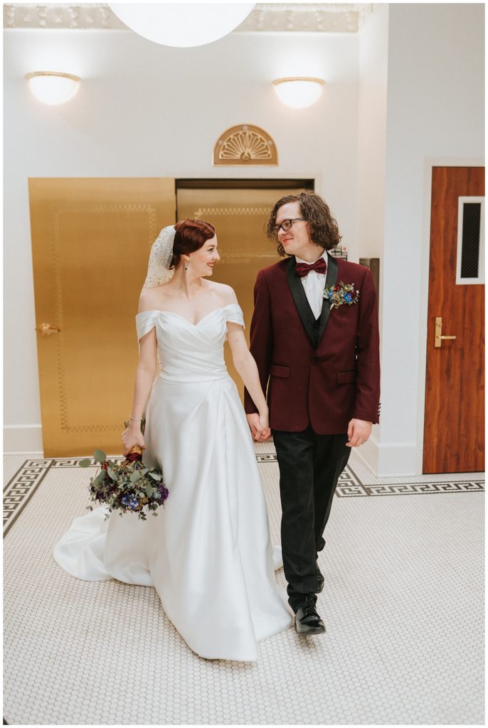 bride and groom walking in front of gold elevator, looking at each other