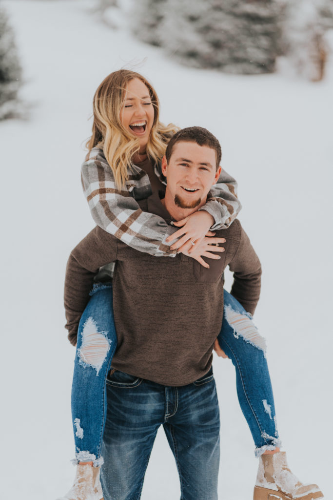 groom gives bride piggy back ride at their snowy engagement session, wedding photographer in twin falls